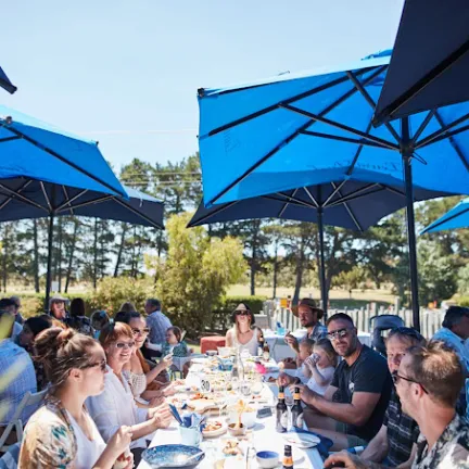 a group of people sitting at a table with a blue umbrella